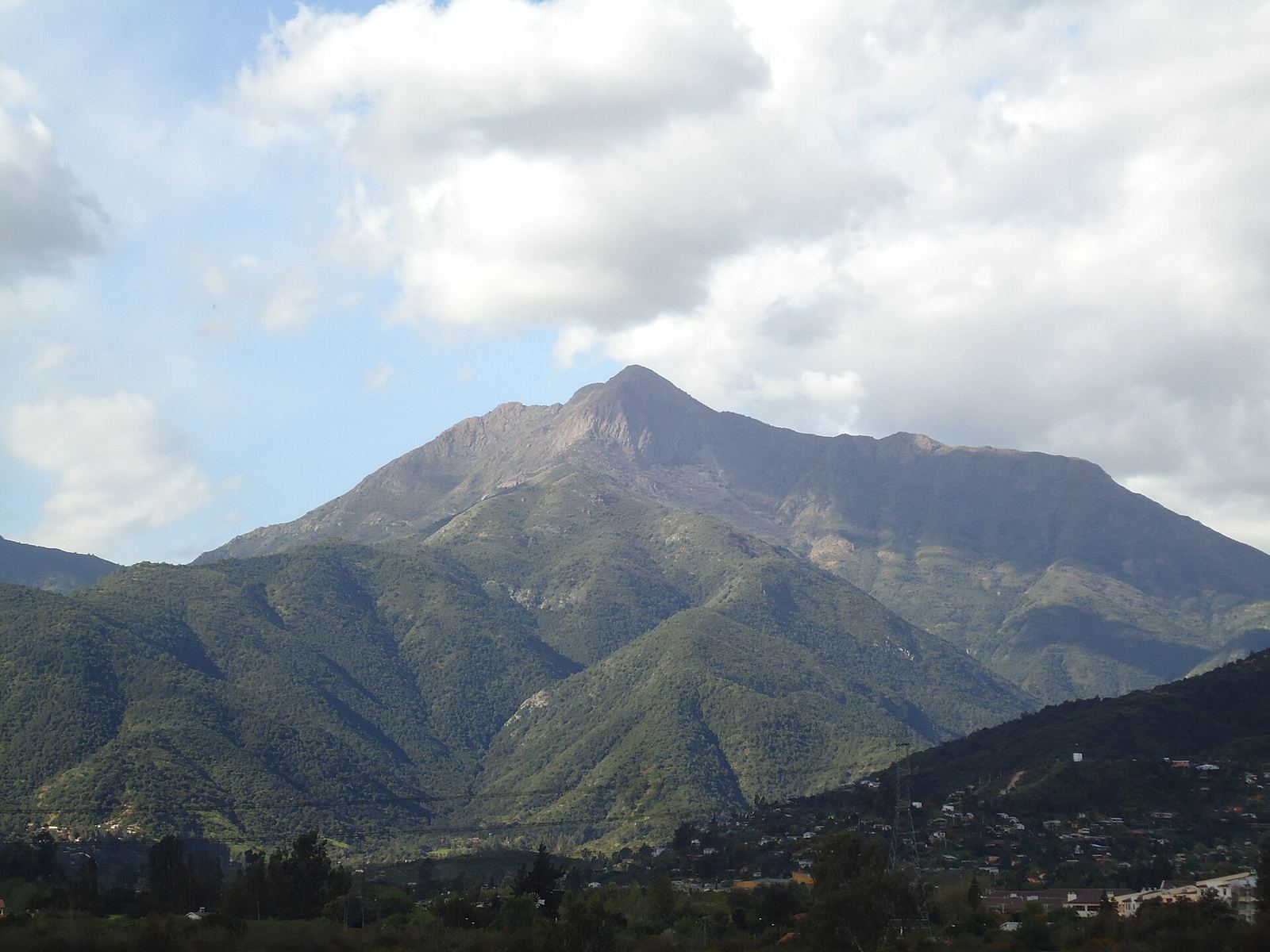 Cerro La Campana bajo nubes blancas, con el valle verde abajo